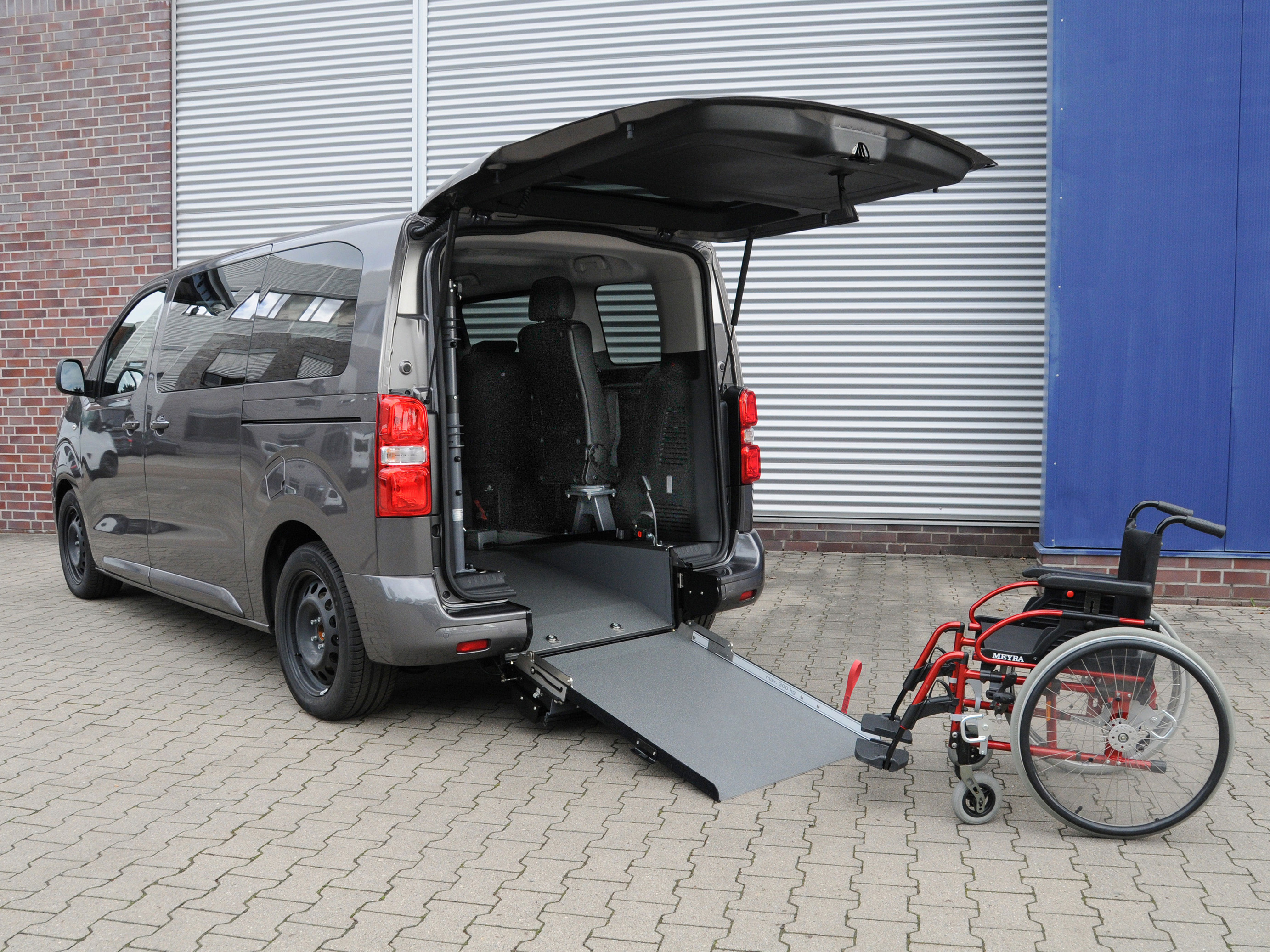 Toyota Proace City L2 Elettrico A con rampa posteriore abbassata e carrozzina davanti all’accesso del vano, configurazione per trasporto disabili