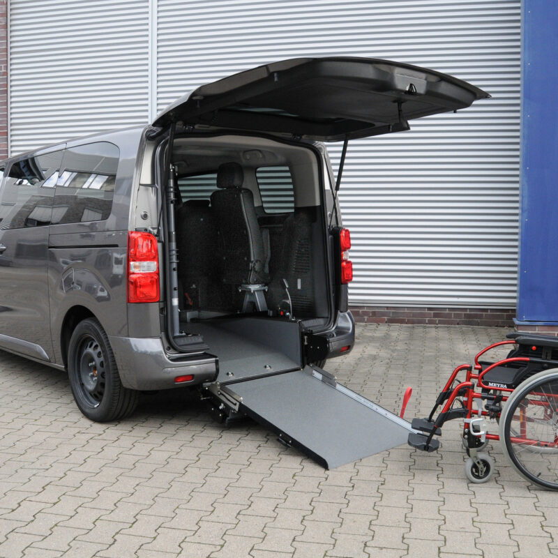 Toyota Proace City L2 Elettrico A con rampa posteriore abbassata e carrozzina davanti all’accesso del vano, configurazione per trasporto disabili