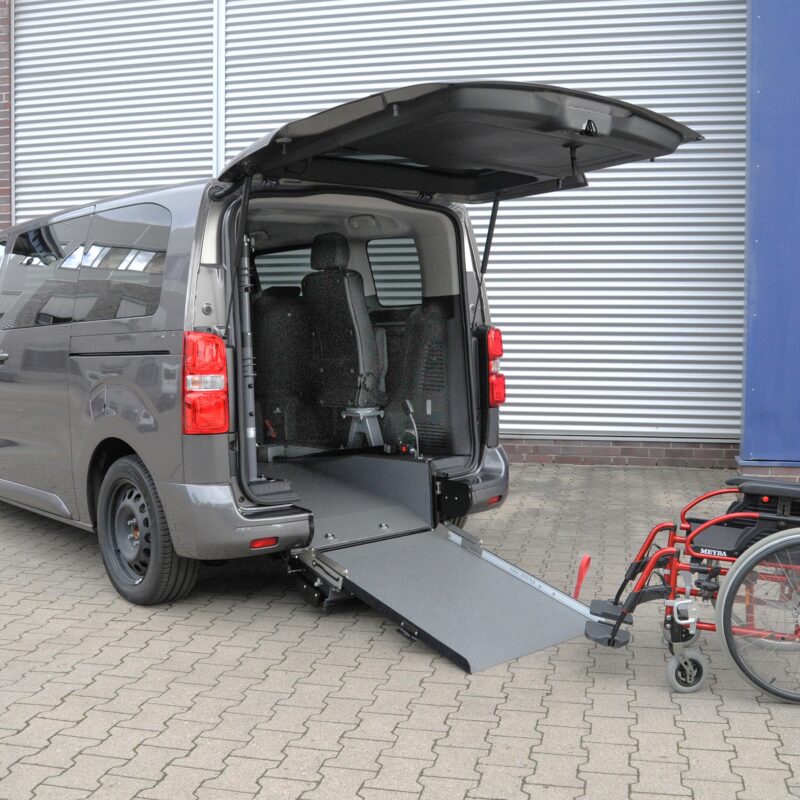 Toyota Proace City L2 Elettrico A con rampa posteriore abbassata e carrozzina davanti all’accesso del vano, configurazione per trasporto disabili.